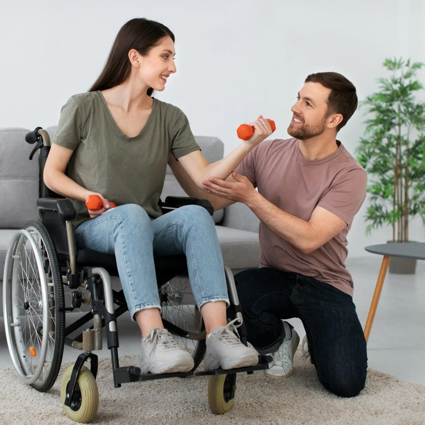 A carer supporting a young woman in a wheelchair with light arm exercises at home